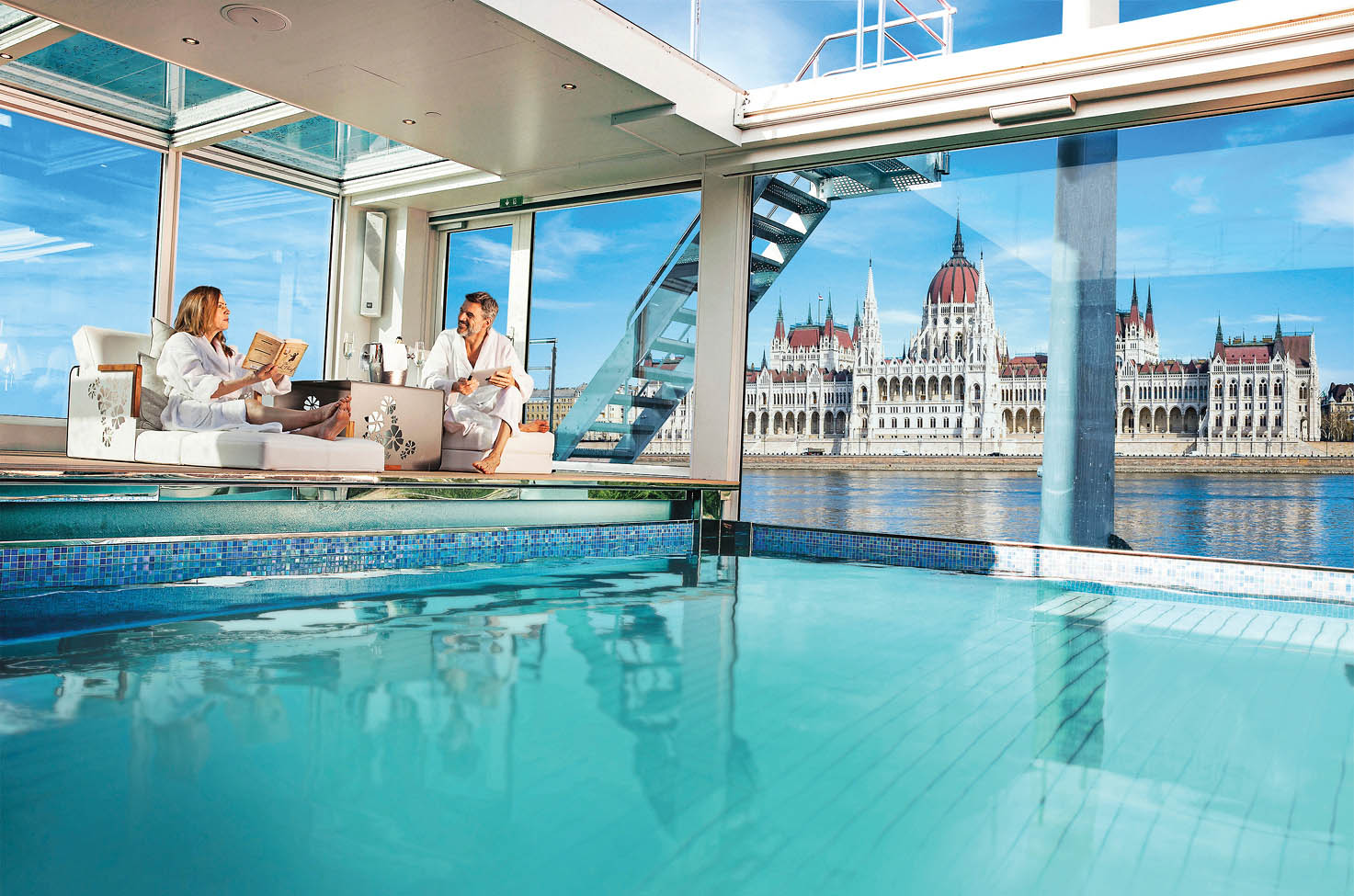 Couple lounging by an on board pool, on a cruise ship sailing past the Hungarian Parliament Building