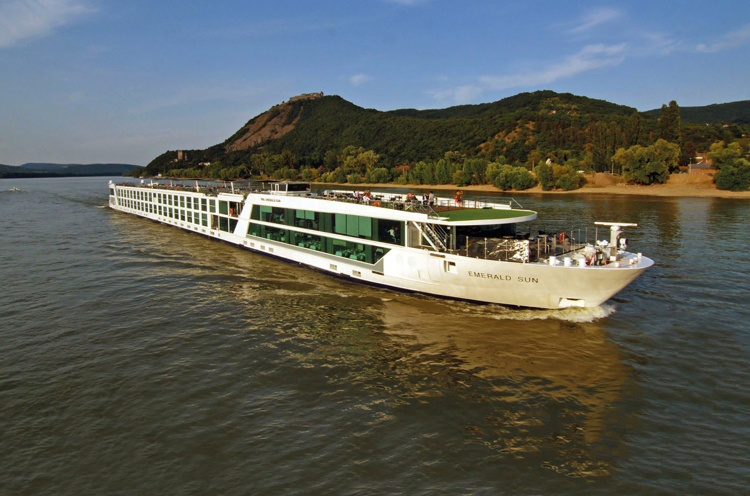 Luxury river cruise ship sailing European river past green landscape at sunset, image reflected in water