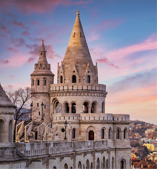 A large stone castle with a pink sky with Fisherman's Bastion in the background