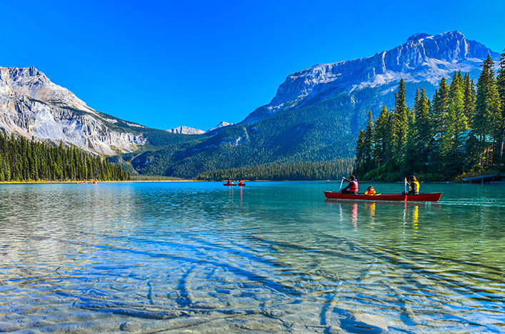People canoeing on lake, surrounded by mountains