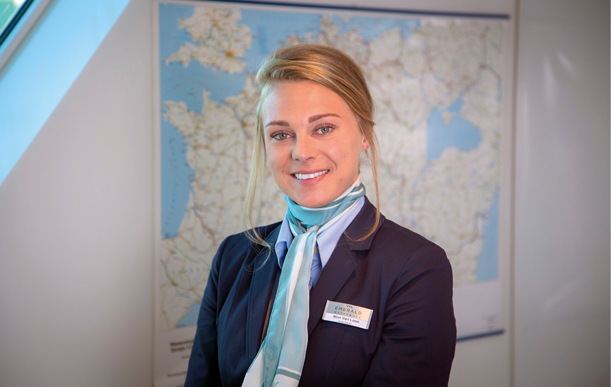 Woman smiling, wearing smart clothing in her office, with a map on the white wall behind her