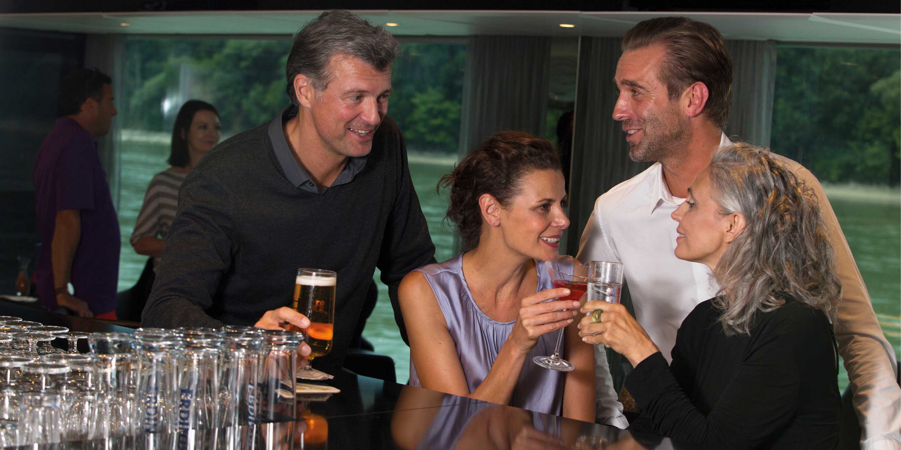 Four people sat at a bar, enjoying their drinks and each other’s company, with river views from the windows behind them