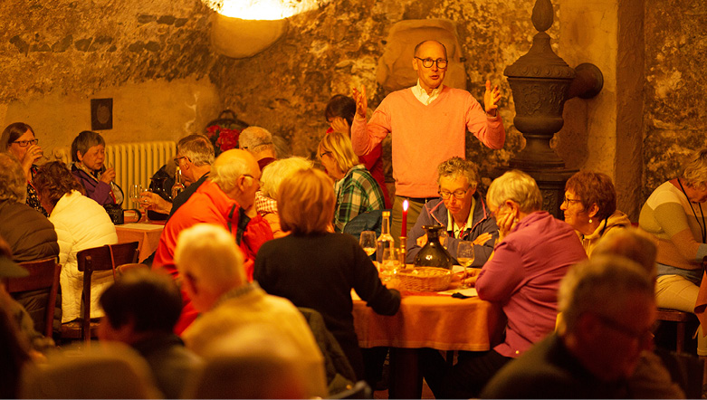 Wine connoisseur hosting a wine tour and tasting session in Bernkastel wine cellar, with many guests seated in the ambiently lit space