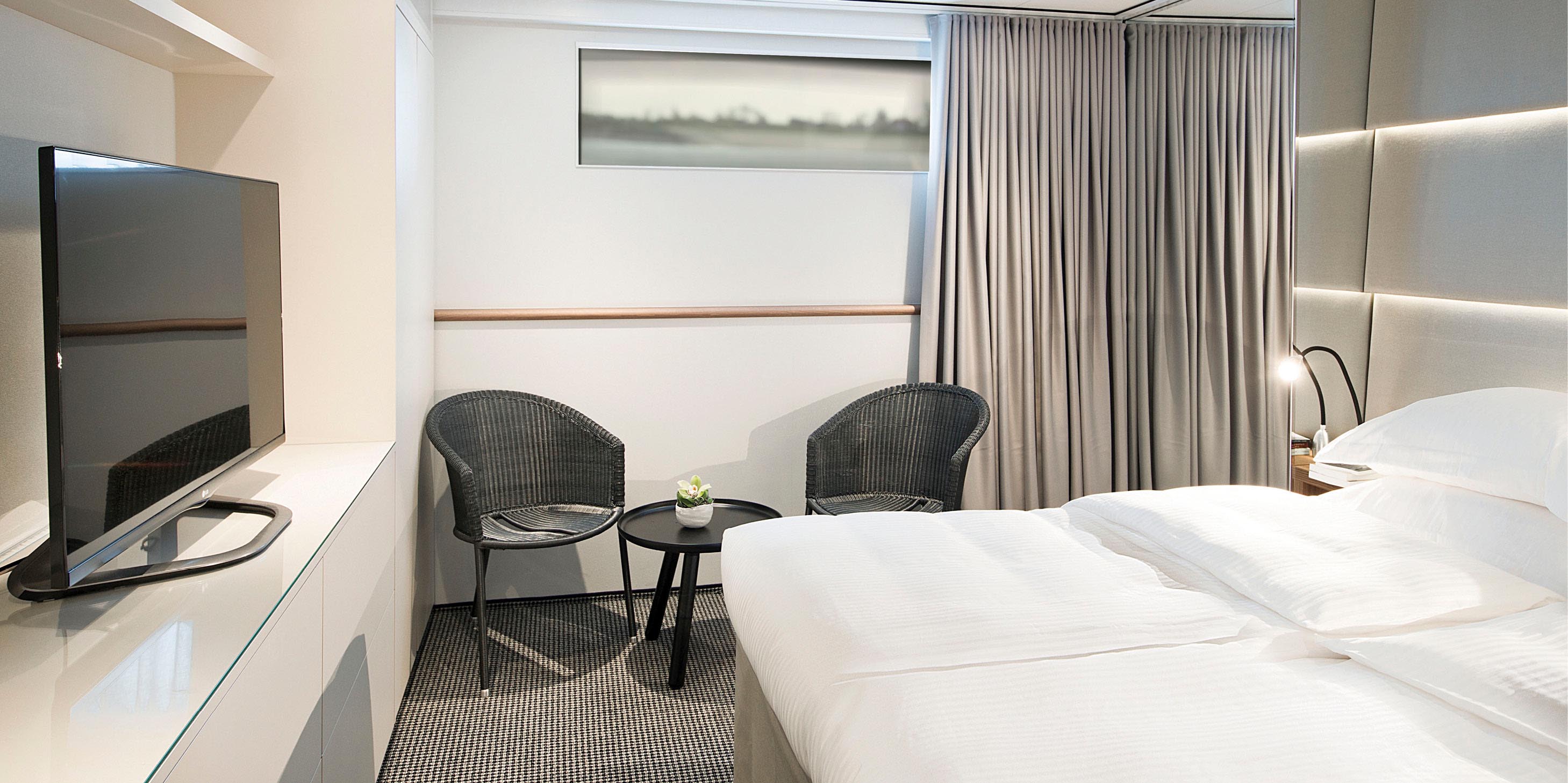 Emerald Stateroom accommodation complete with large bed, seating, flat-screen TV, and portside window views