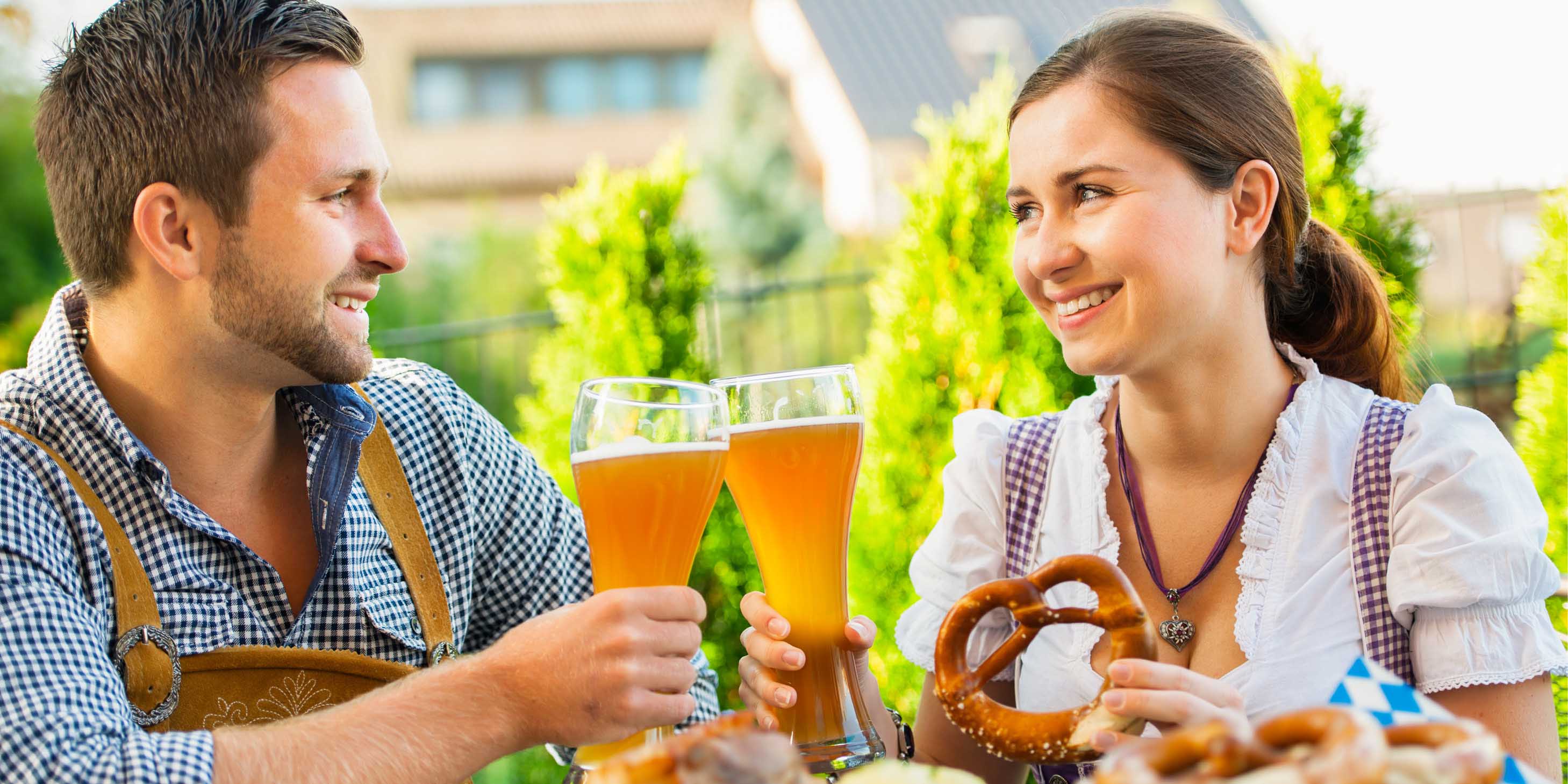 Man and woman drinking a pint of beer and eating a pretzel in traditional Bavarian clothes