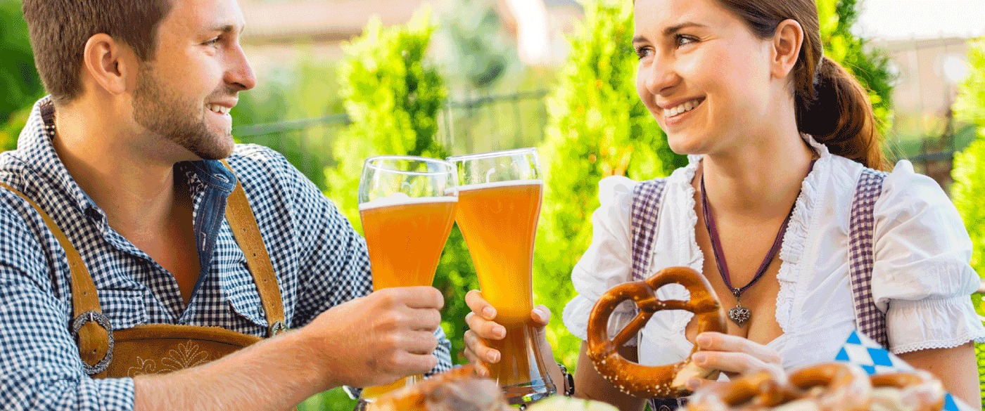 Man and woman drinking a pint of beer and eating a pretzel in traditional Bavarian clothes