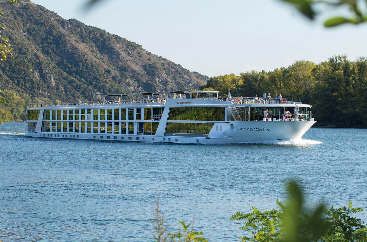 River cruise ship sailing the Rhone River past trees and hills