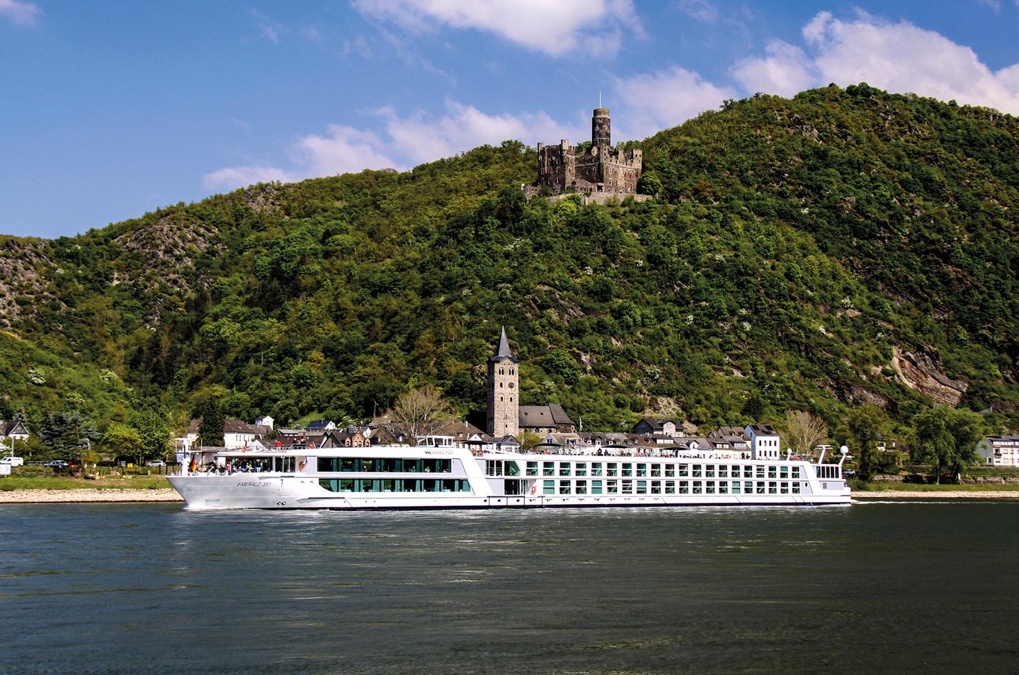 River cruise ship sailing calm blue waters past green hills with a castle in background