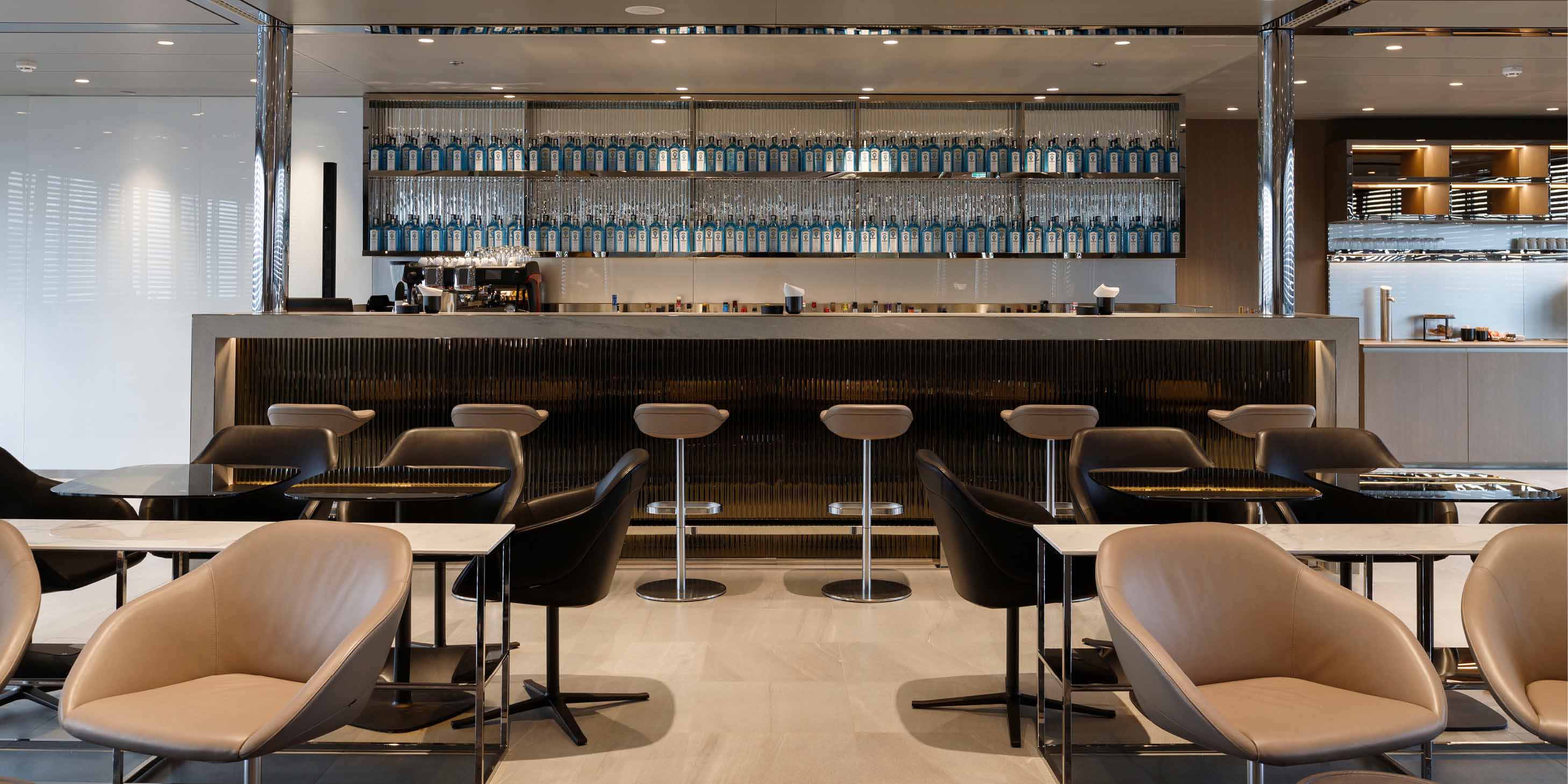 A well-stocked bar with rows of bottles and comfortable stools, with tables and additional seating in the foreground 