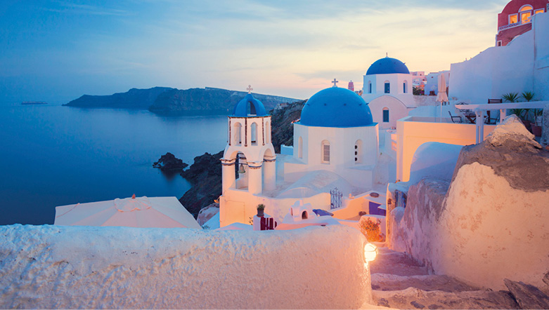 Whitewashed buildings with blue domes at dusk overlooking the tranquil southern Aegean Sea
