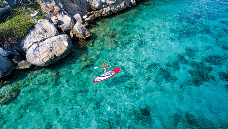 Aerial view of a woman enjoying paddleboarding on the clear blue waters of the Caribbean Sea along the rocky coastline