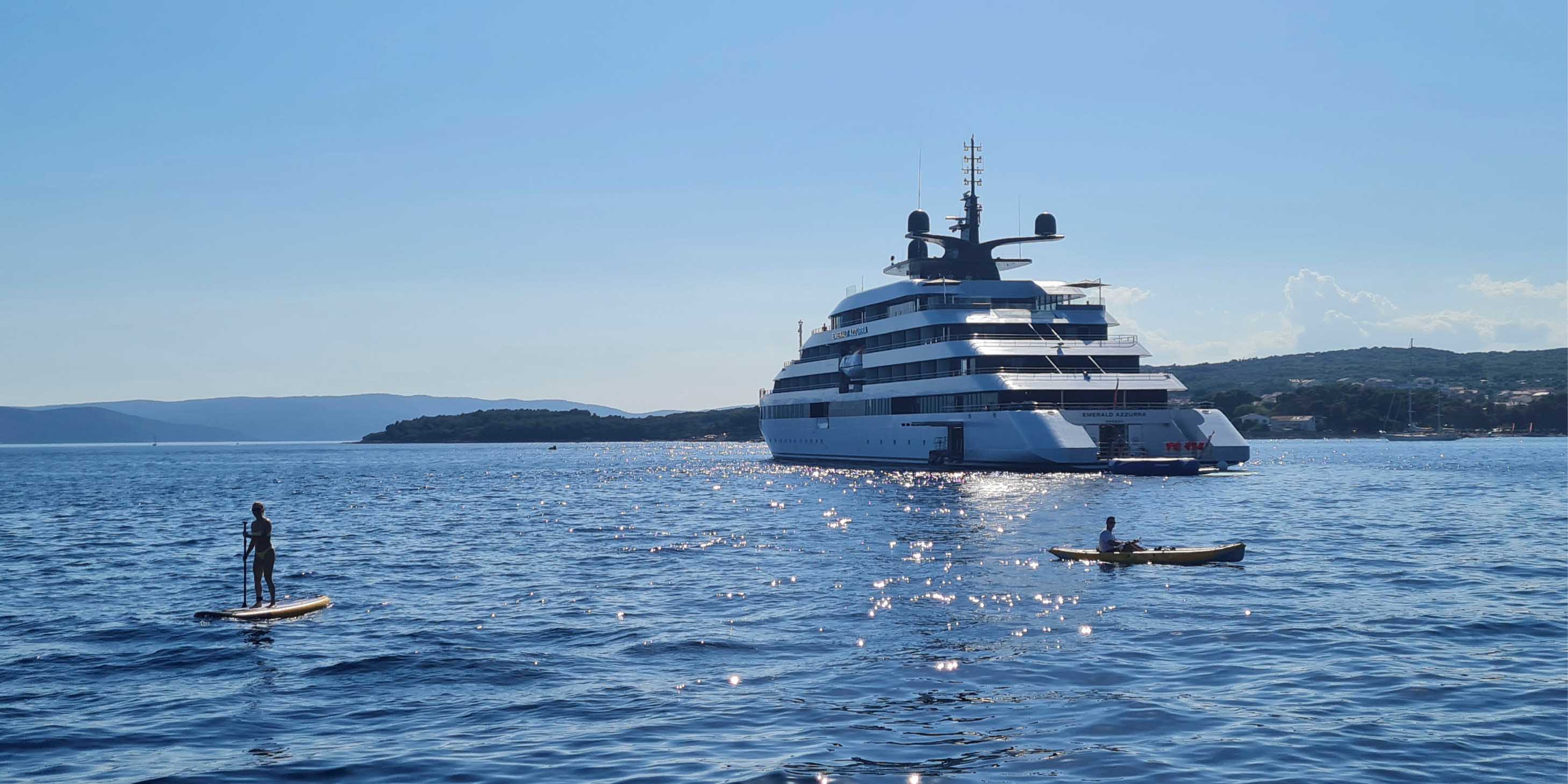 People paddleboarding and kayaking in the calm sea next to an Emerald Cruises luxury yacht