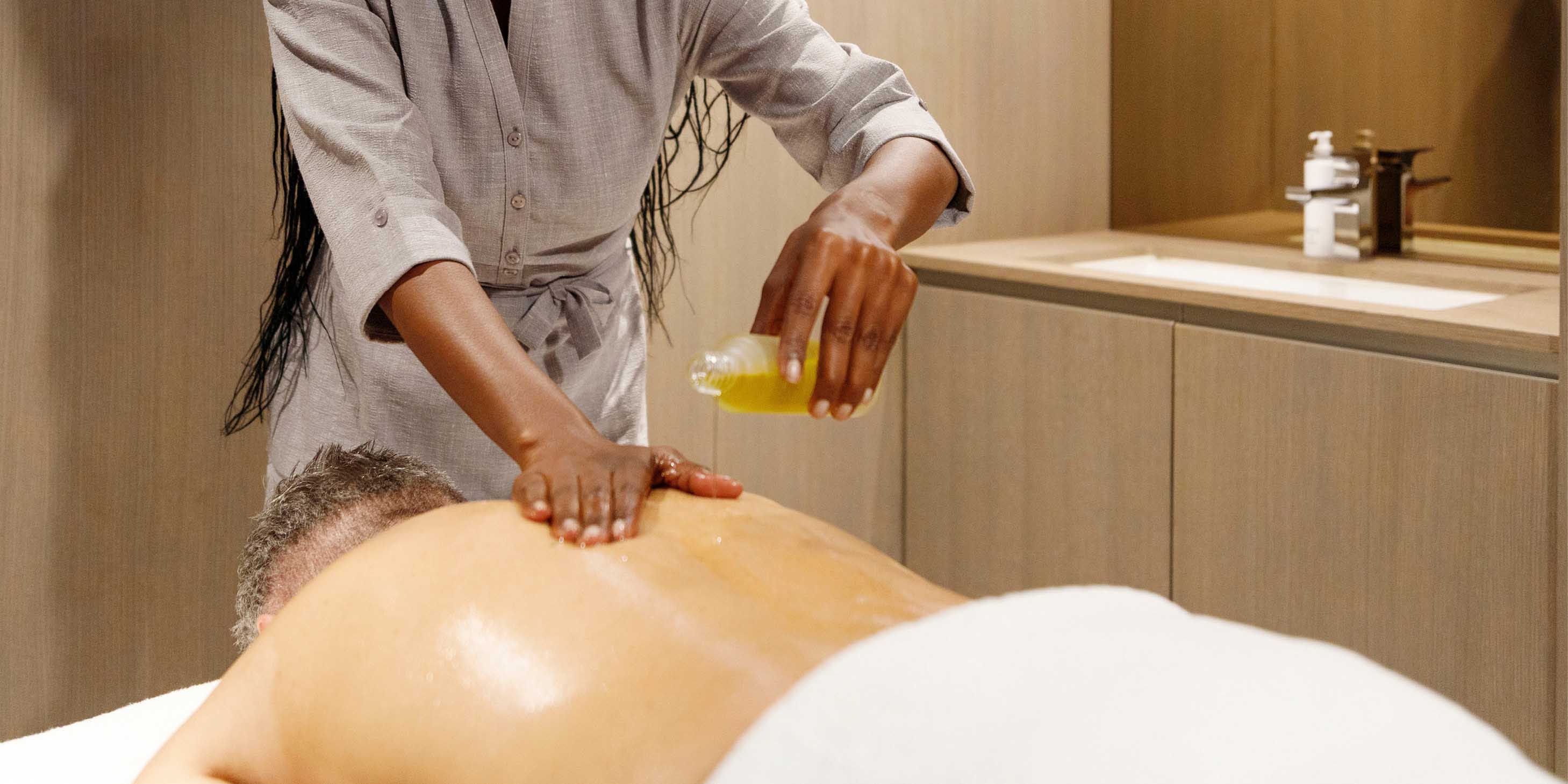 A massage therapist pouring ESPA luxury oils for a guests’ back massage in massage therapy room