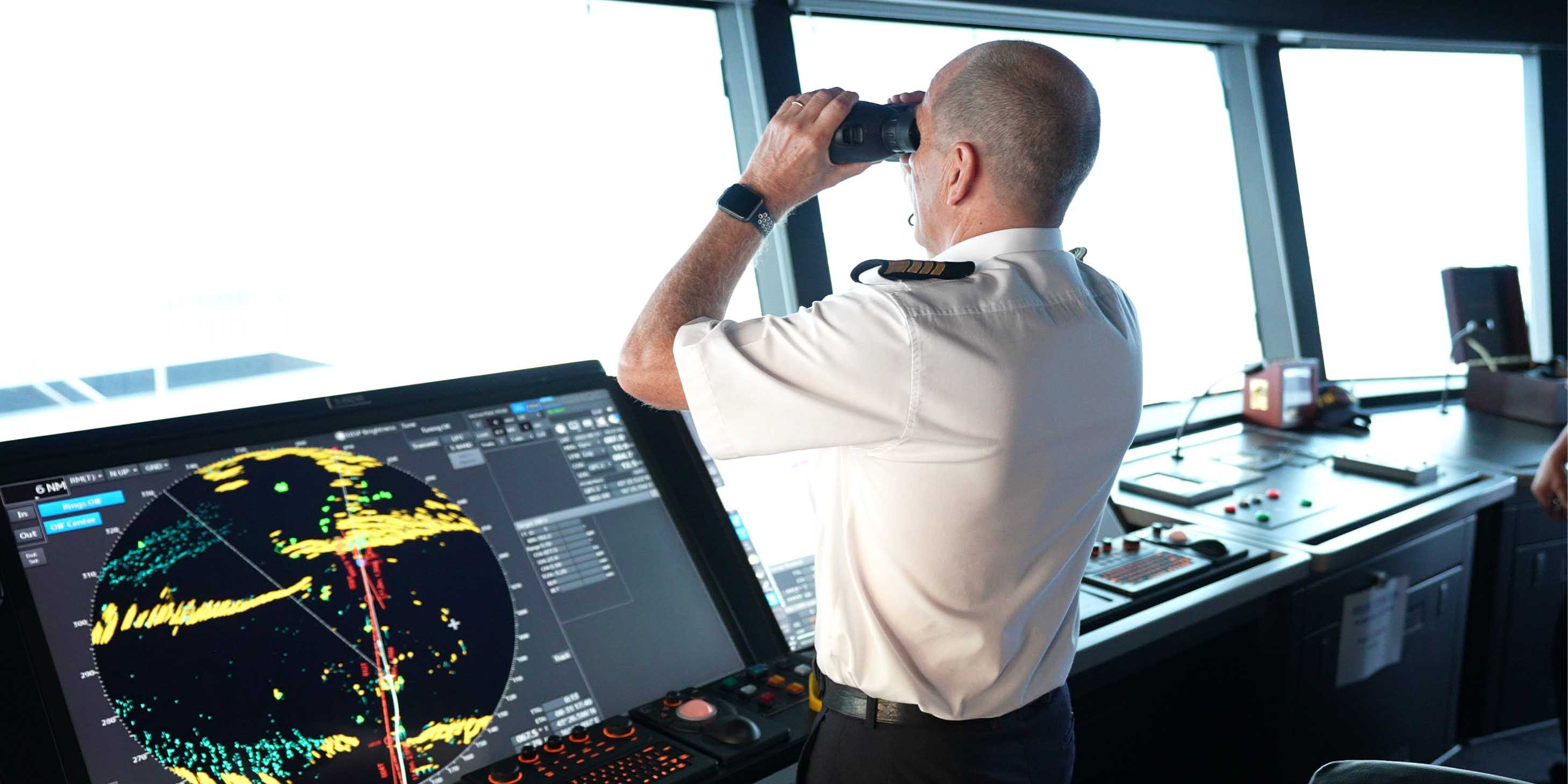 Captain looking out of binoculars towards the horizon from the navigation bridge of an Emerald Cruises luxury yacht cruise